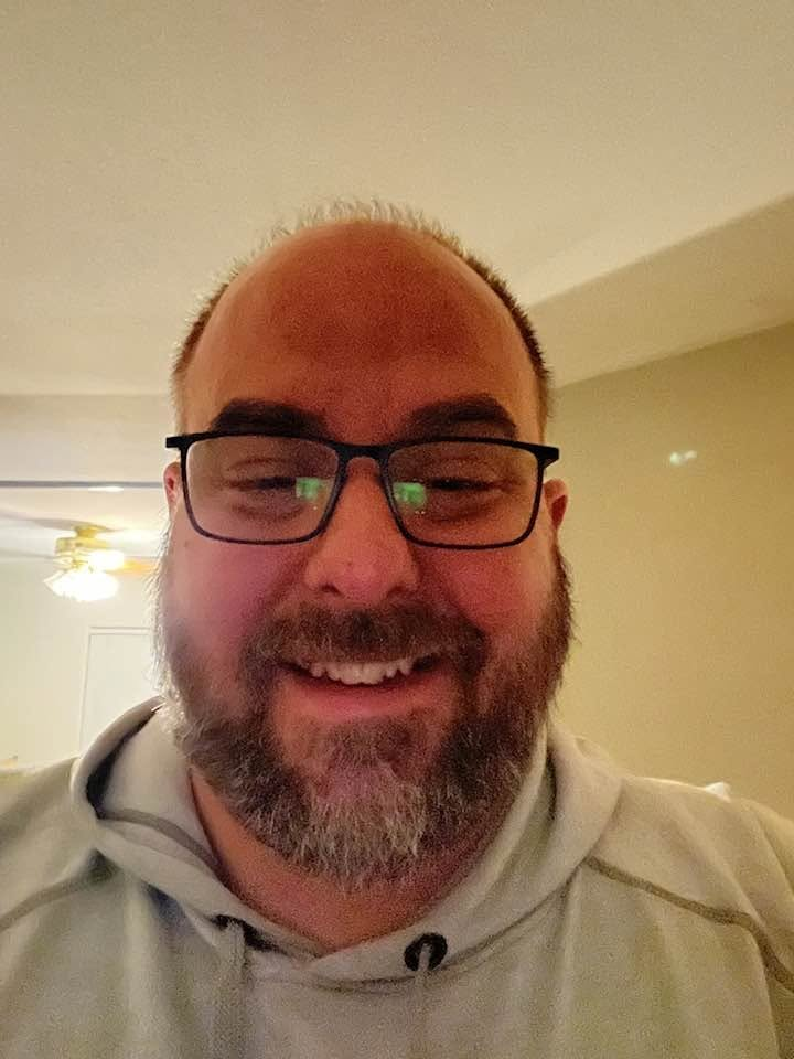 Michael DeMarois smiling, wearing glasses and a gray hoodie